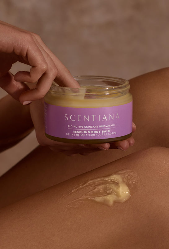 A woman holding a jar of Rescuing Body Balm, applying it to her legs