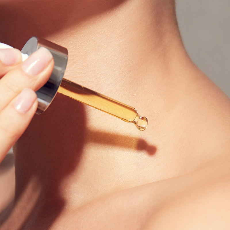 Hand holding a dropper with oil above skin of her décolletage