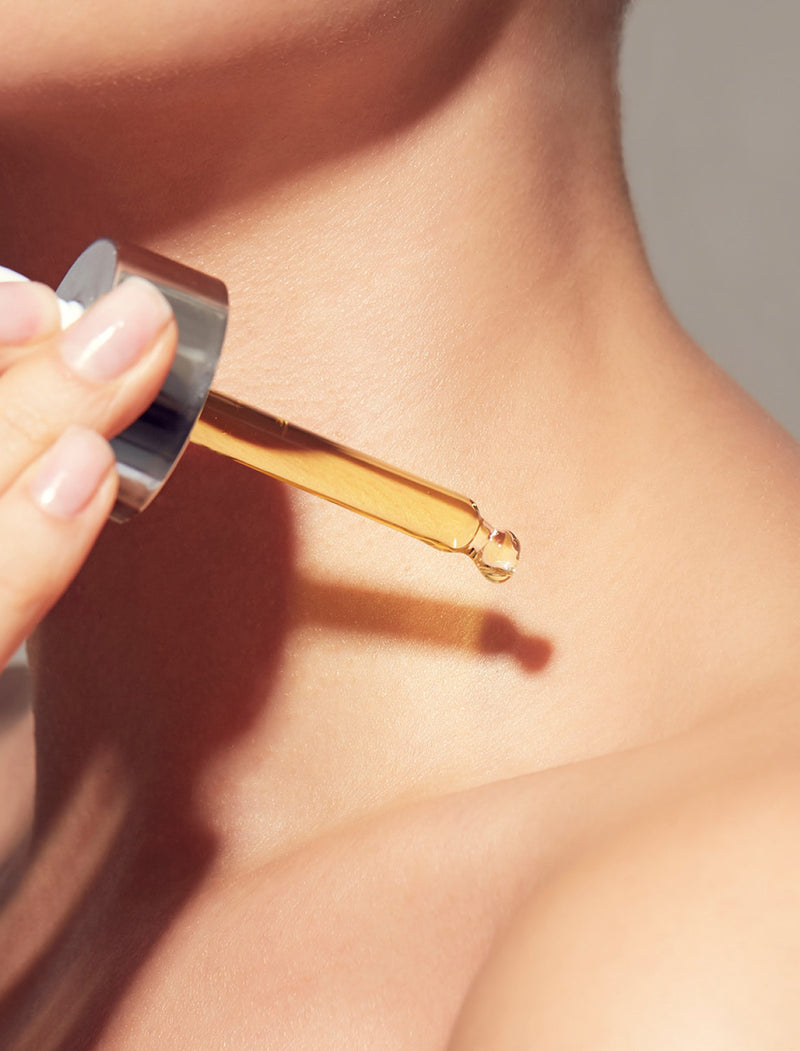 Hand holding a dropper with oil above skin of her décolletage