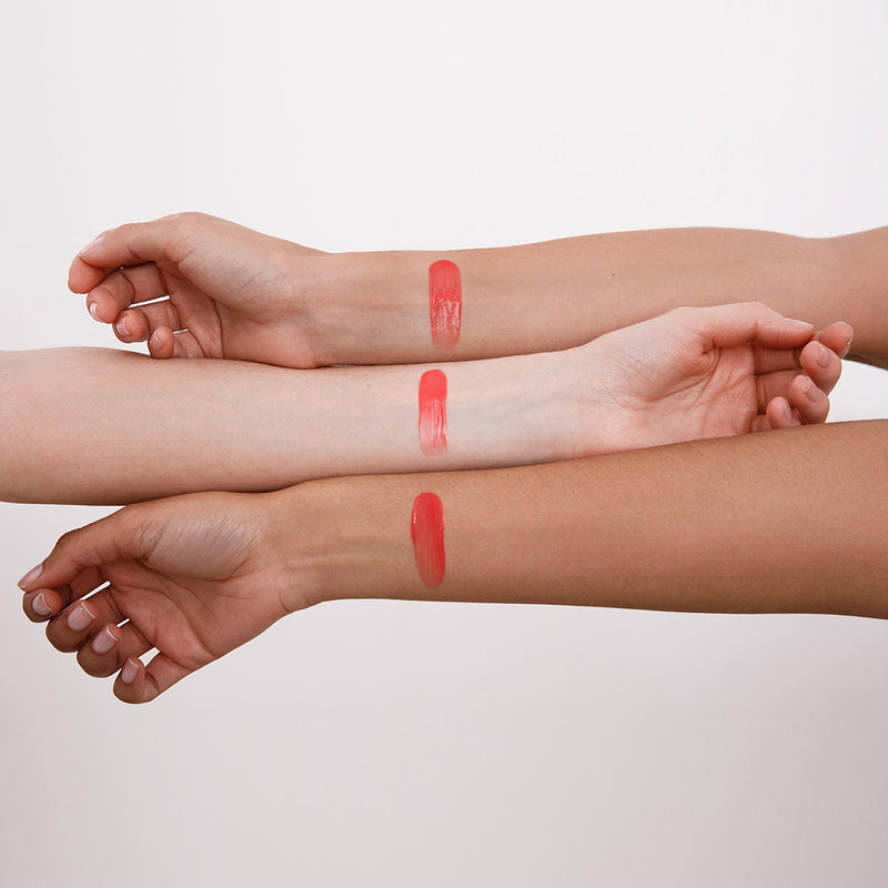 Three swatches of a red lip gloss on arms of different skin tones.
