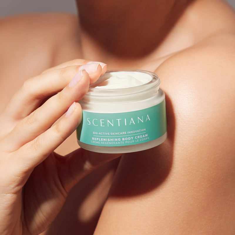 Hand holding a jar of Scentiana body cream against shoulder