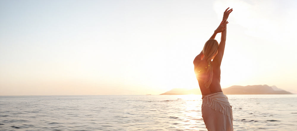 Woman stretching with arms outstretched over a body of water at sunset