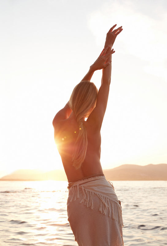 Woman stretching with arms outstretched over a body of water at sunset
