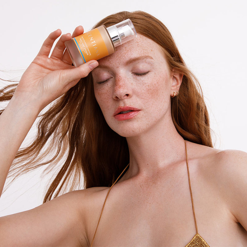 Woman Holding Sunlit Body Shimmer Bottle To Her Forehead